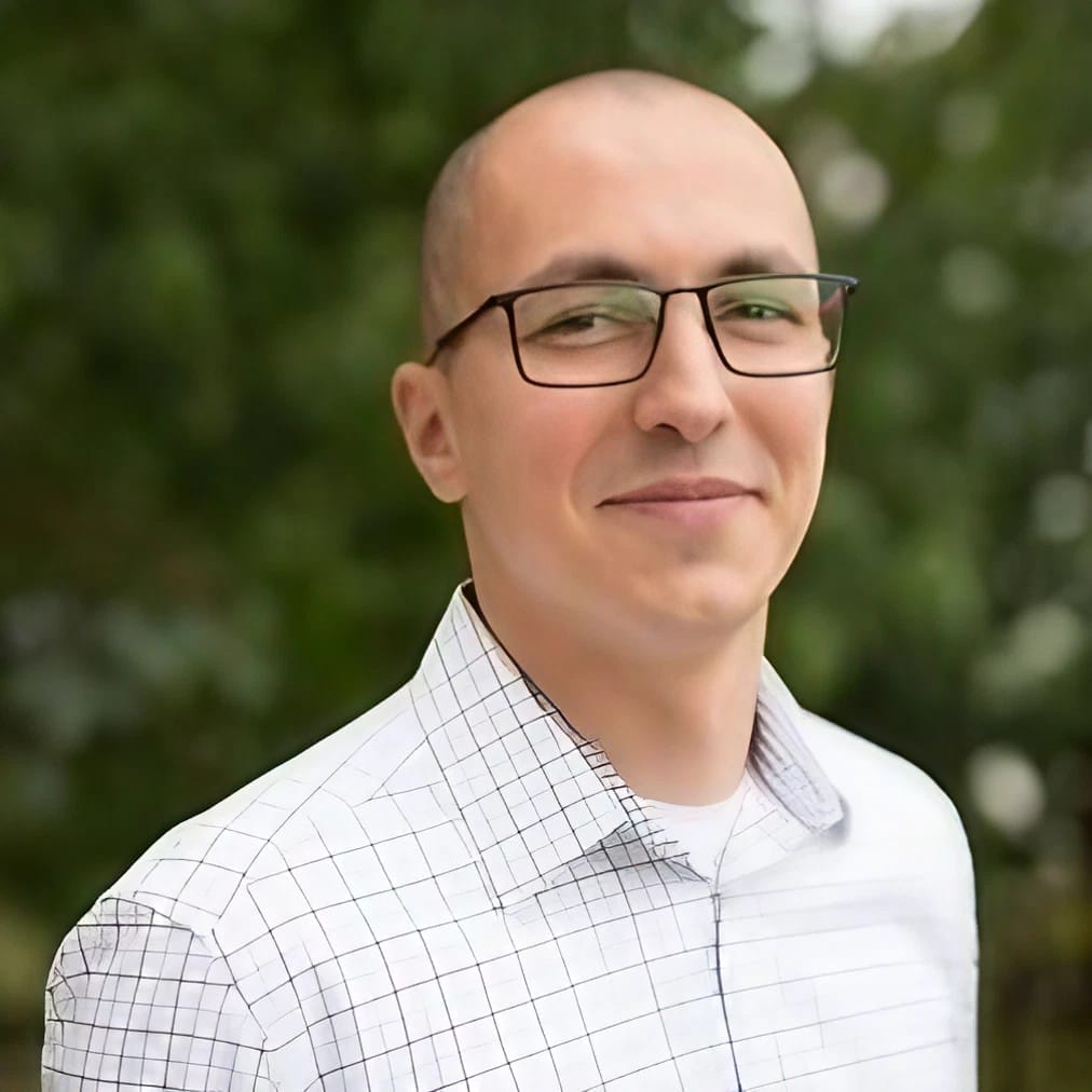 Man smiling outdoors wearing glasses and white shirt.
